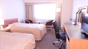 Une chambre d’hôtel avec deux lits, un bureau, une chaise, une télévision et une fenêtre avec des rideaux.