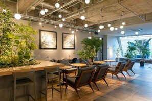 Een moderne binnenruimte met tafels, stoelen, planten en lijstwerken aan de wanden.