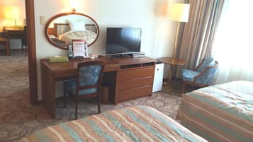 A hotel room with a bed, a desk with a television, a chair, and a lamp.