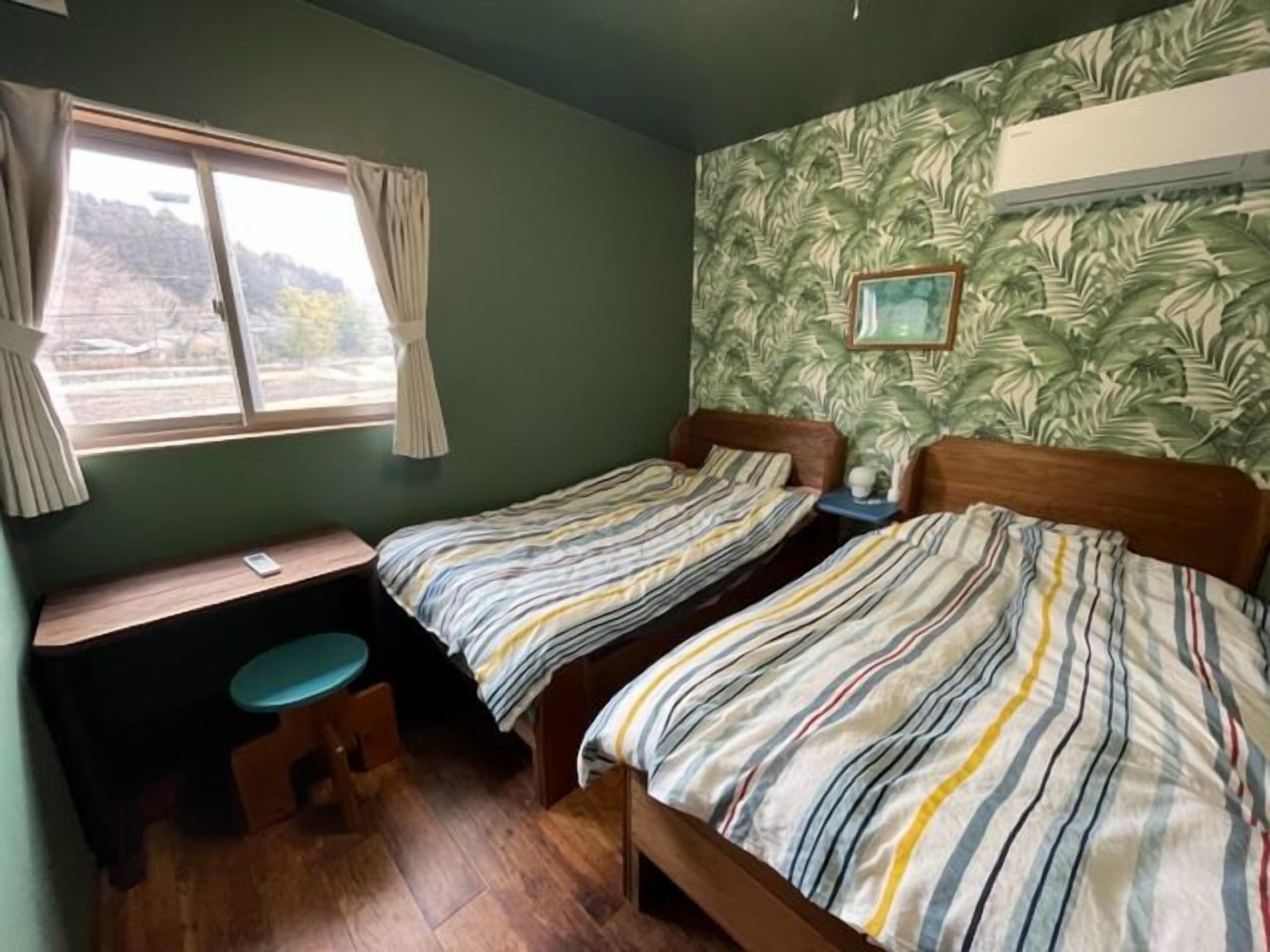 Een kamer met twee enkele bedden, een klein bureau, een stoel en een raam met gordijnen.