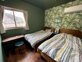 Una habitación con dos camas individuales, un escritorio pequeño, una silla y un ventanal con cortinas.