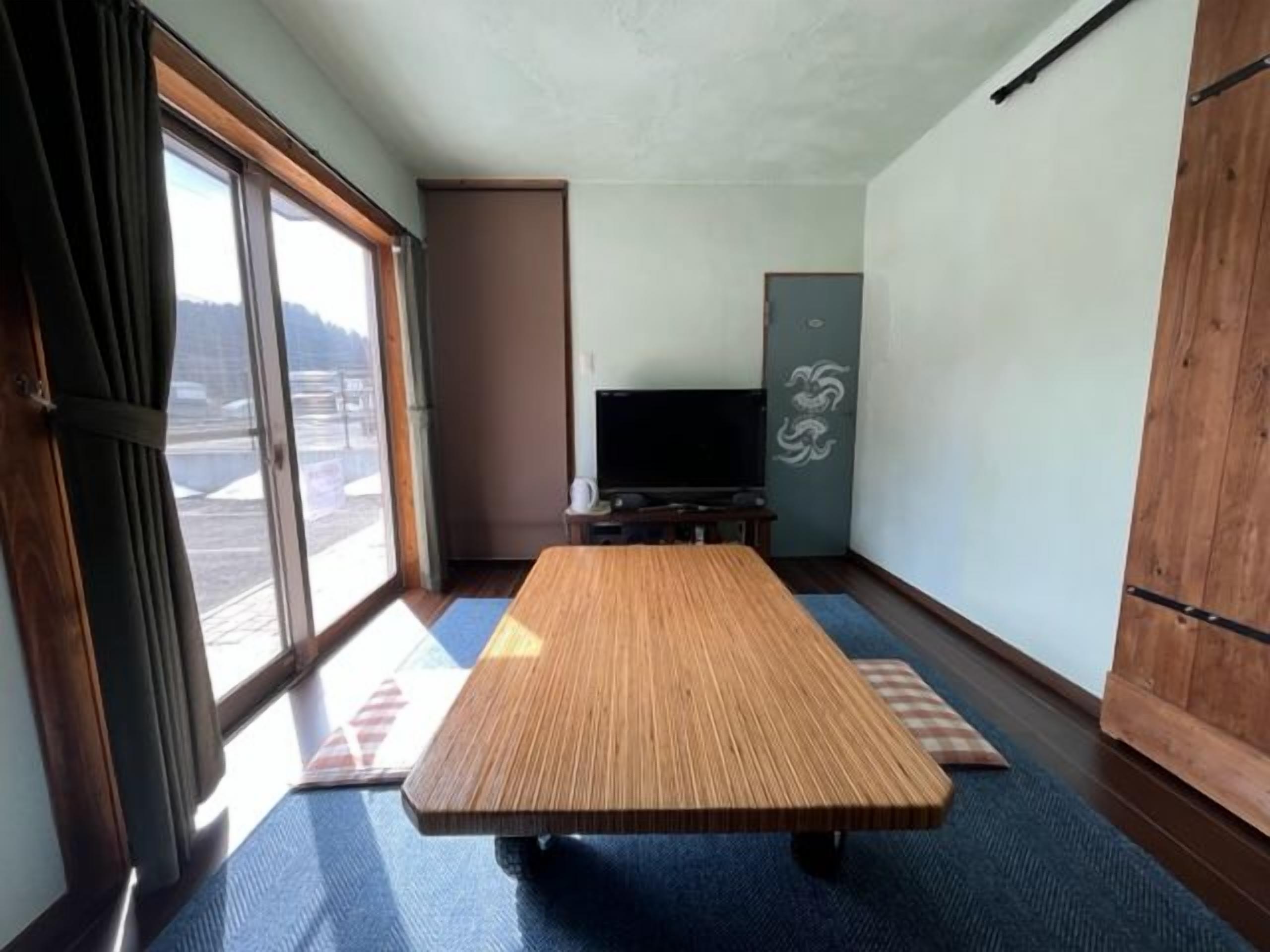 A room with a tatami mat table, a television, and a sliding door leading to a balcony.