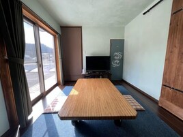 Una habitación con una mesa de tatami, televisión y puerta corredera que da a un balcón.