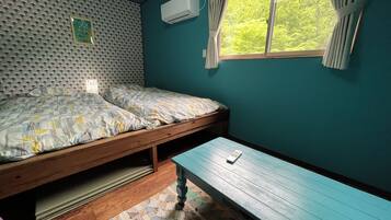 A room with two beds, a window with curtains, an air conditioning unit, and a wooden bench.