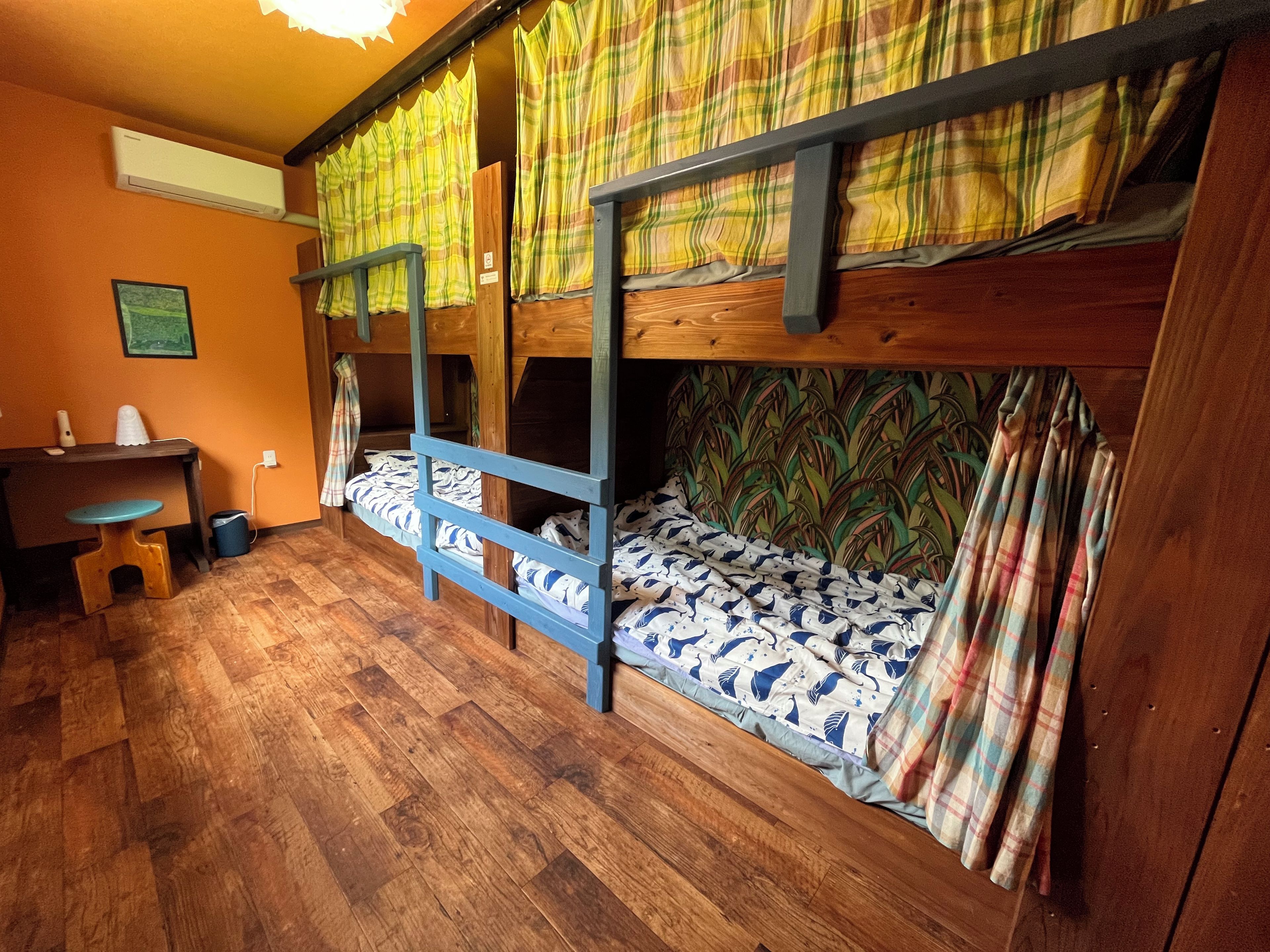 Een slaapkamer met stapelbed, houten vloer, bureau en stoel.