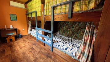 Een slaapkamer met stapelbed, houten vloer, bureau en stoel.