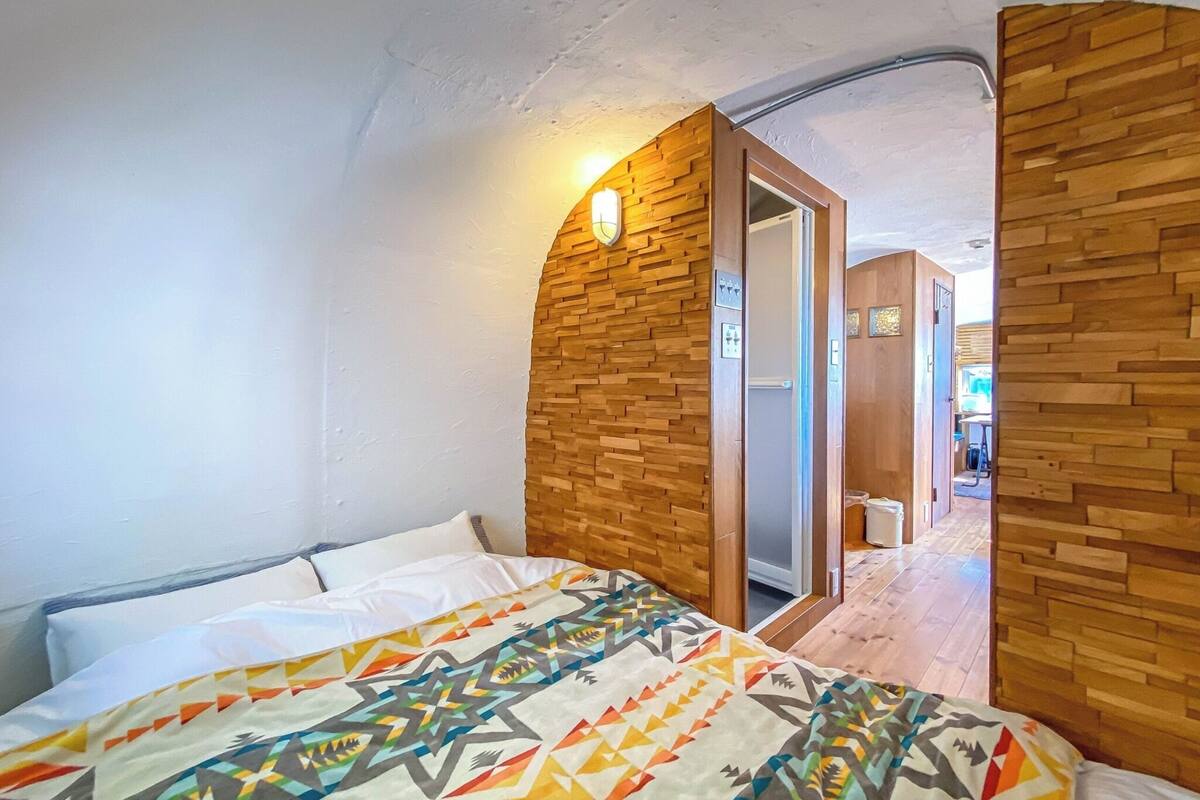 A bedroom with a bed, wooden wall paneling, and a door leading to another room.