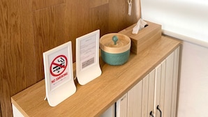 A wooden wall with a framed picture, a no-smoking sign, a menu, and a small wooden table with a bowl. - Isola Base Awaji (Awaji)