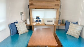 A compact room with a wooden table, a window with blinds, a small kitchenette, and two blue cushioned seating areas. - Isola Base Awaji (Awaji)