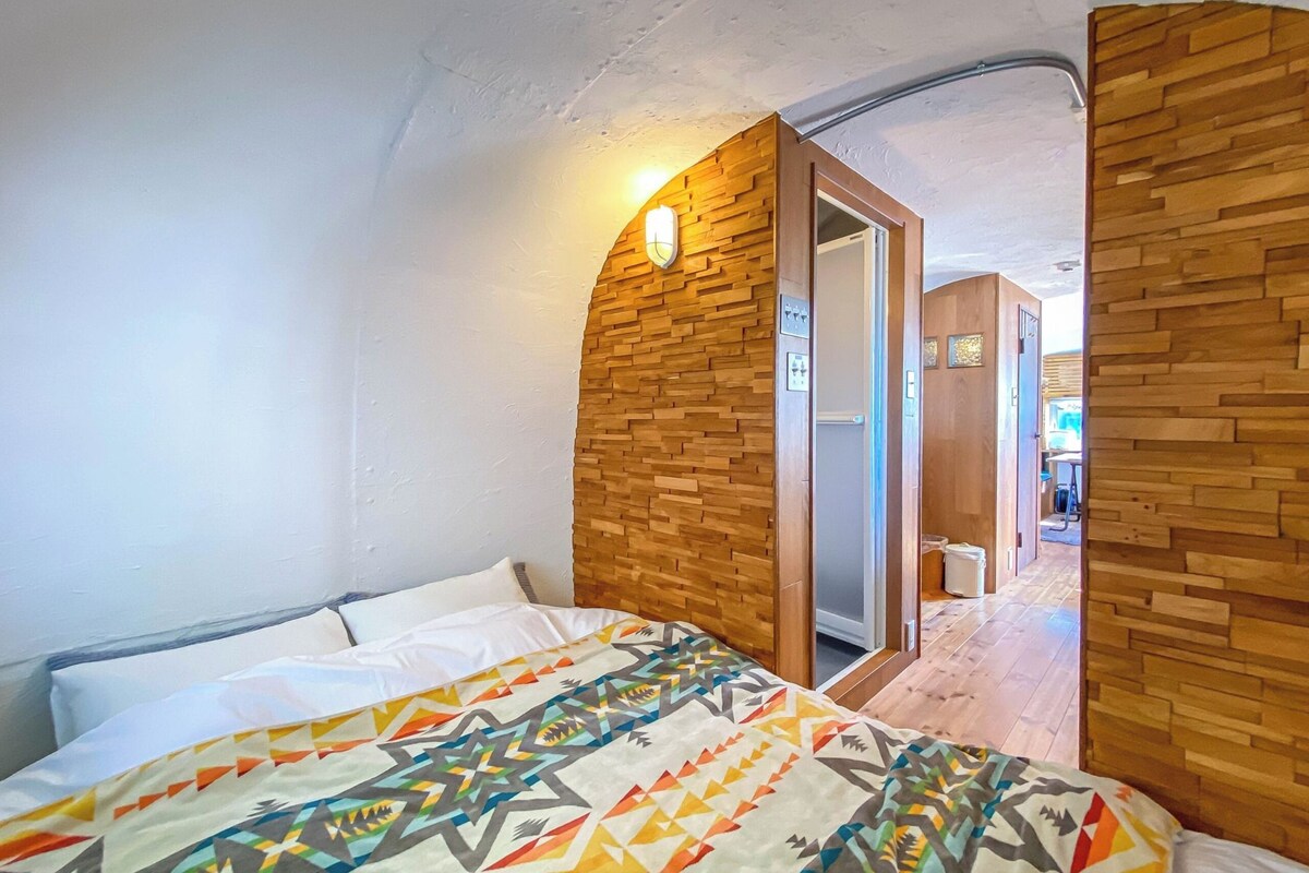 A bedroom with a bed, wooden wall paneling, and a door leading to another room.