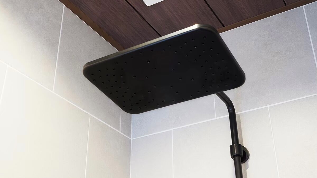 A showerhead in a corner of a room with white tiled walls and a wooden ceiling.