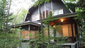 Een huis met twee verdiepingen, met een donkere gevel, omgeven door dicht bos.