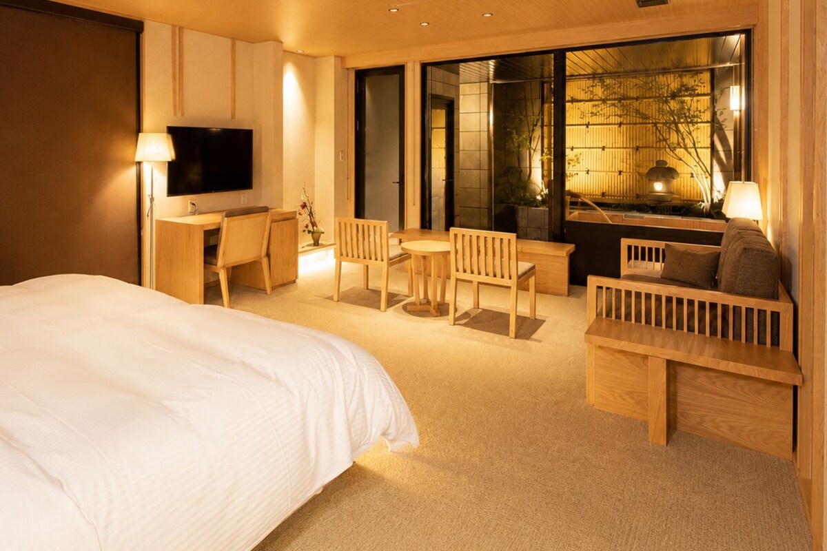 A hotel room with a large bed, a desk with a chair, a television, and a seating area with a table and chairs.