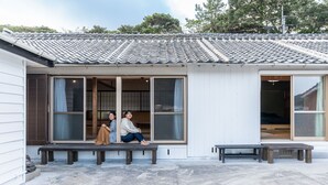 Ein traditionelles japanisches Haus mit einem Ziegeldach, großen Schiebetüren und einer Bank davor.