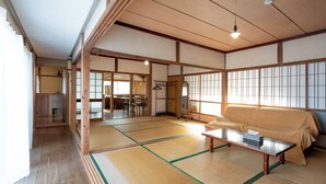 Ein traditioneller japanischer Raum mit Tatami-Boden, einer Tatami-Matratze als Sofa, einem niedrigen Holztisch und Schiebetüren zu weiteren Räumen.
