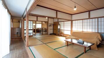 Una habitación japonesa tradicional con suelo de tatami, un sofá cubierto de tatami, una mesa de madera baja y puertas correderas que dan a otras estancias.
