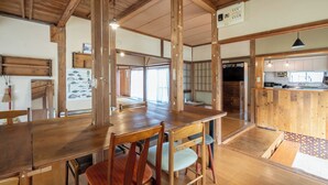 Ein traditioneller japanischer Raum mit Tatami-Bodenbelag, Holzmöbeln und einem durch einen offenen Durchgang einsehbaren Küchenbereich.