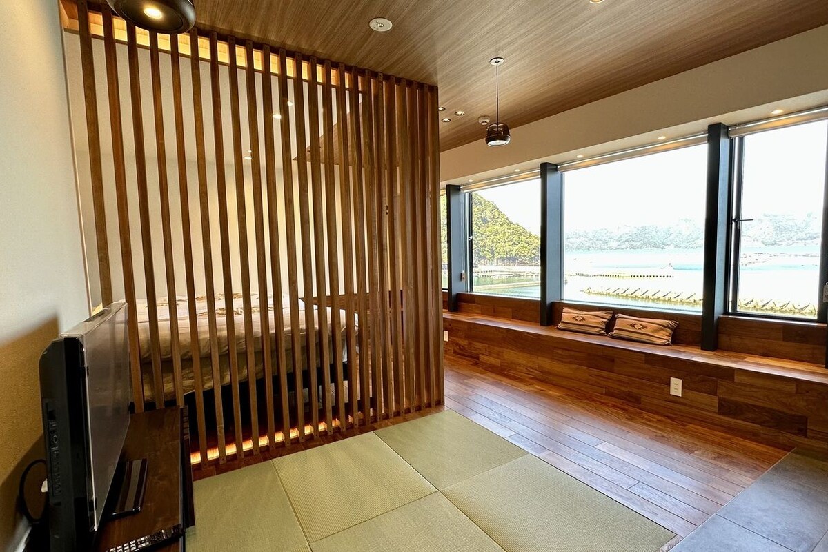 A modern room with a wooden slat partition, a large window with a view of a beach, and a built-in bench with cushions.