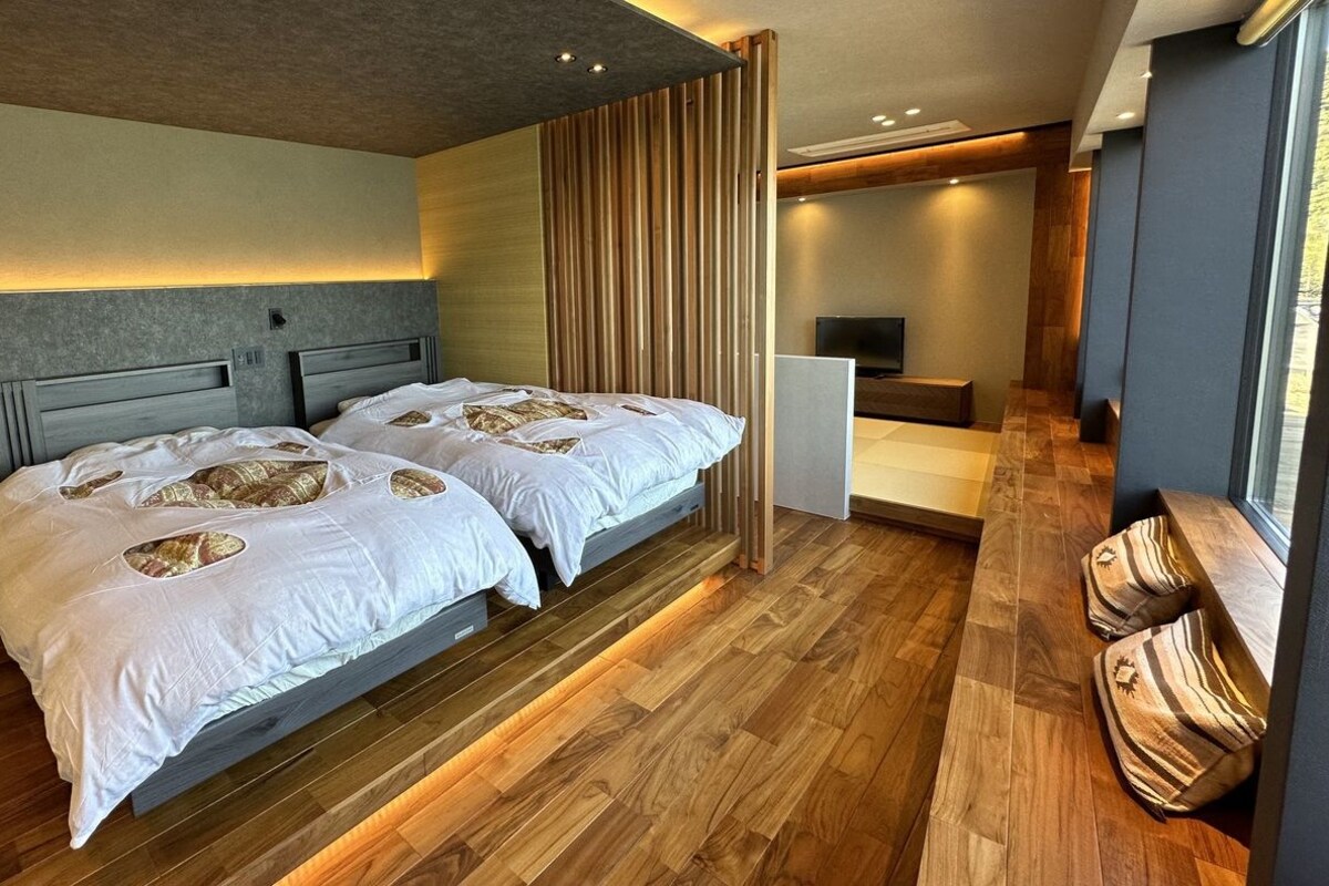 A modern hotel room with two beds, a TV, and a wooden floor.