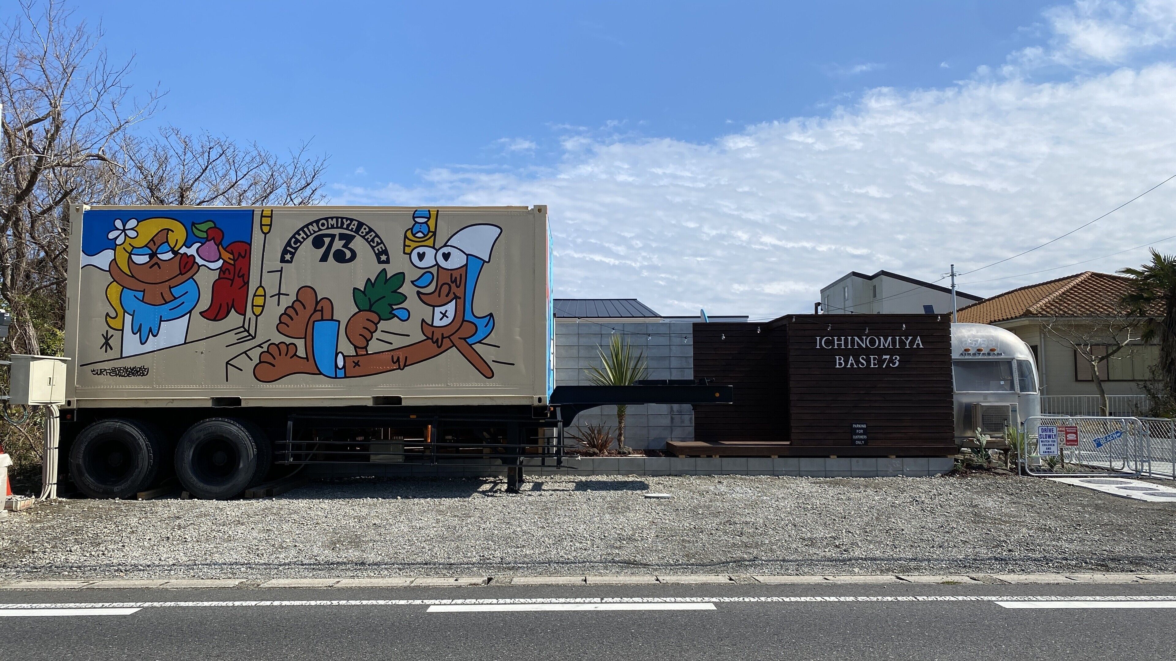Un camion orné d’une publicité colorée est garé devant un bâtiment portant l’inscription « ICHINOMIYA BASE 73 ».