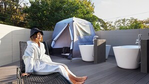 A person seated on a chair on a deck with a tent and two tubs. - Maigre Flat (Ito)