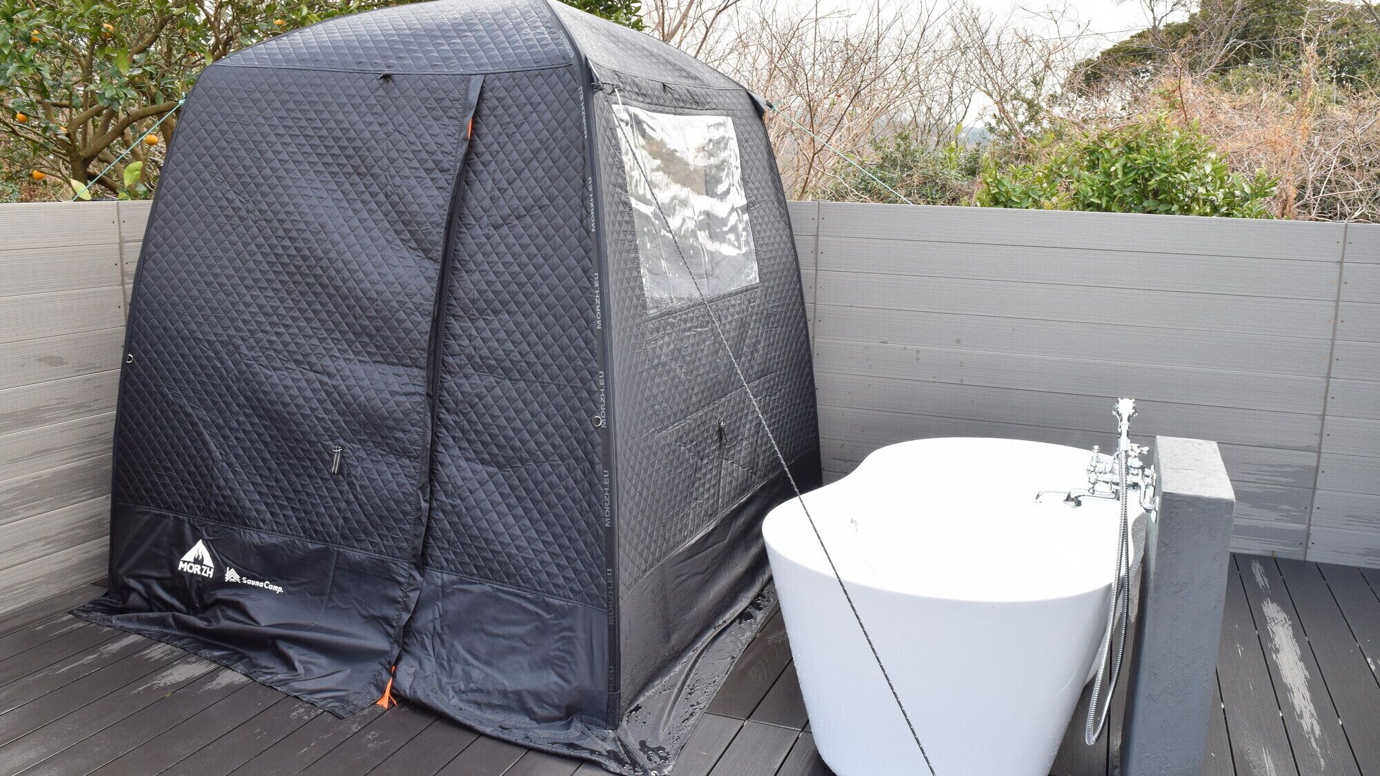 Una carpa portátil con interior blanco, una bañera blanca y una terraza de madera.