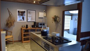 A compact kitchen with a gas stove, a coffee maker, and a microwave. There is a wooden chair and a small table with a vase of flowers. - Maigre Flat (Ito)