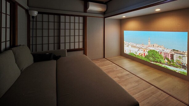 A bedroom with a large bed, a view of a cityscape through a window, and a traditional Japanese shoji screen. - Maigre Flat (Ito)