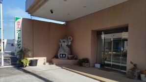 Une entrée d’immeuble ornée d’une sculpture en pierre, de plantes en pot et d’une enseigne en japonais.