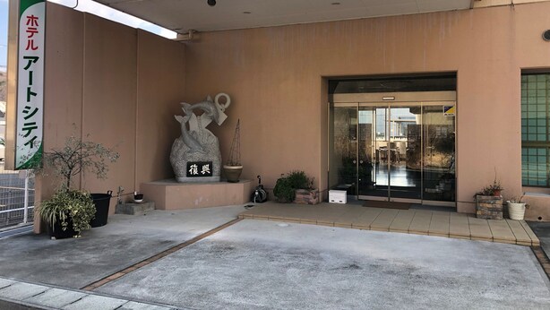 Une entrée d’immeuble agrémentée d’une grande sculpture, d’une plante en pot et d’une enseigne.