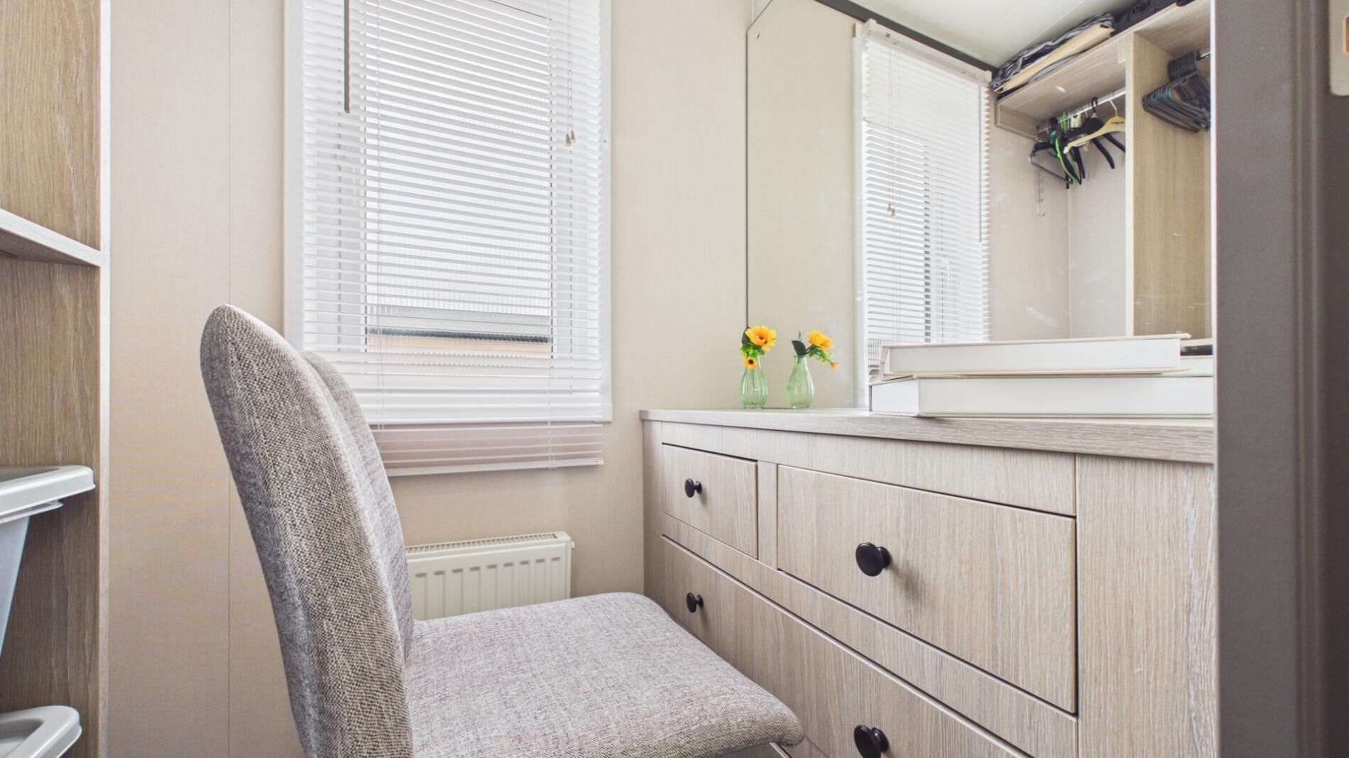 A bathroom with a chair, a vanity with a mirror, and a radiator.