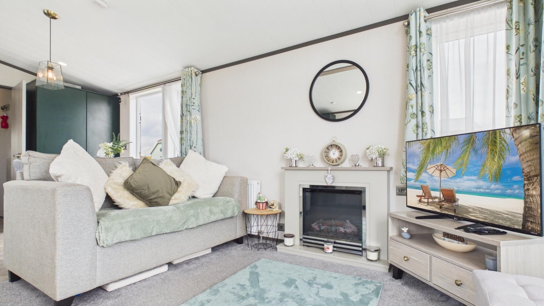 A living room with a sofa, television, fireplace, and a painting of a beach scene.