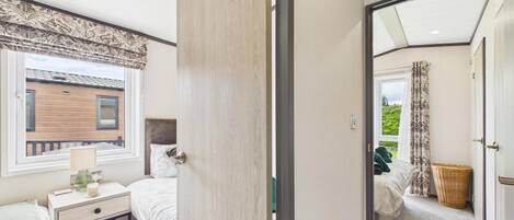 Un dormitorio con cama, mesita de noche, lámpara y ventana con cortinas.