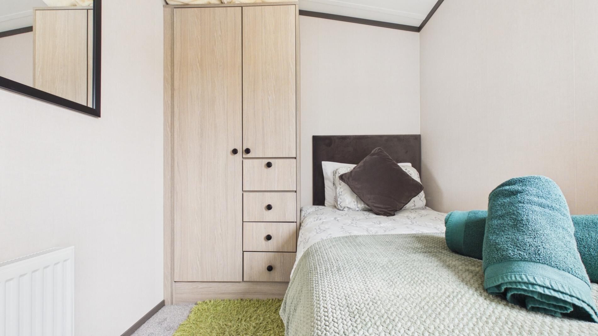 A bedroom with a bed, a wardrobe, a radiator, and a mirror.