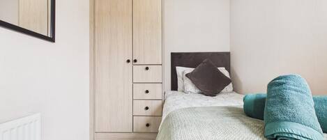 A bedroom with a bed, a wardrobe, a radiator, and a mirror.