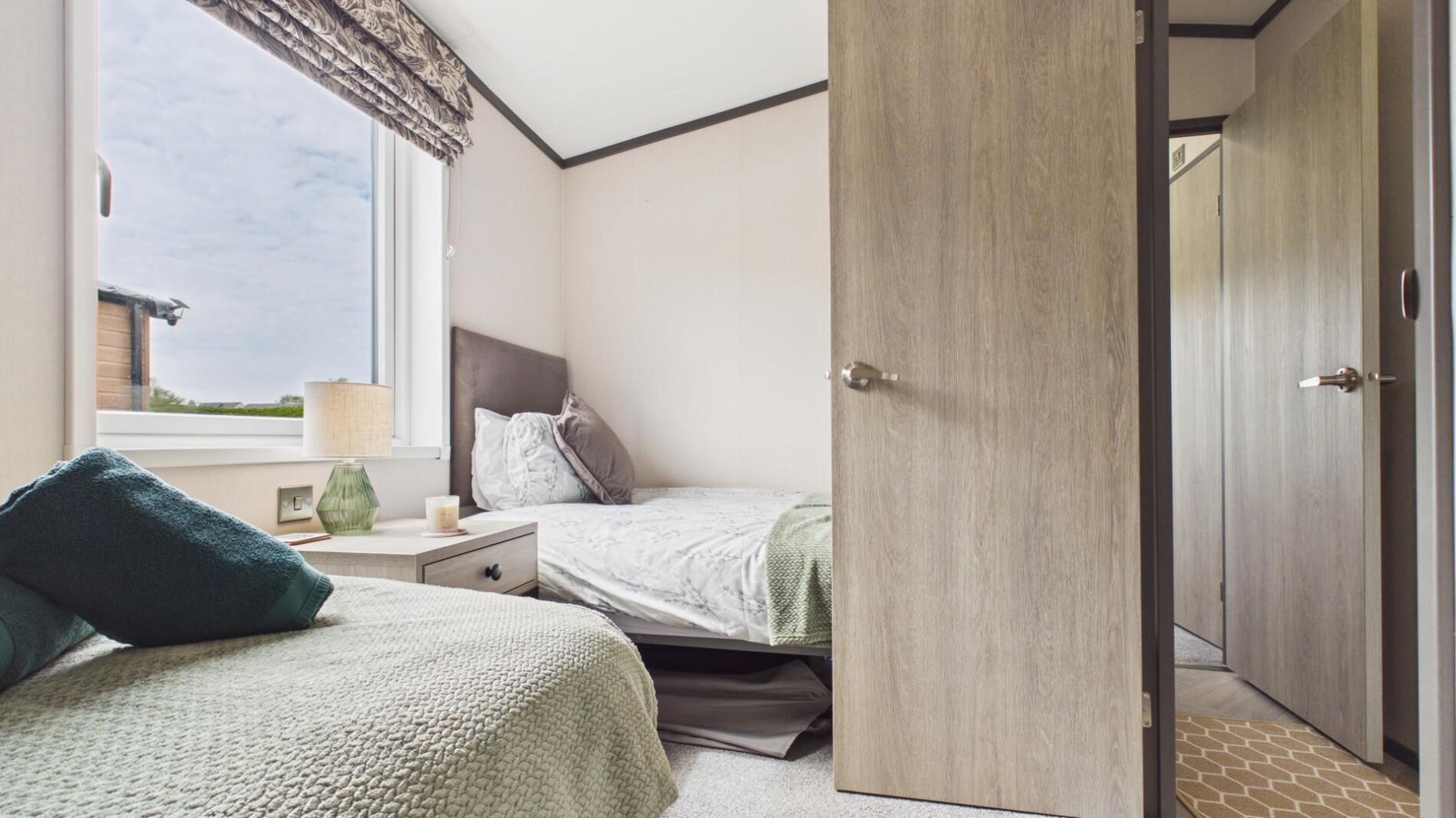 A bedroom with a bed, bedside table, lamp, and a view of the outside.