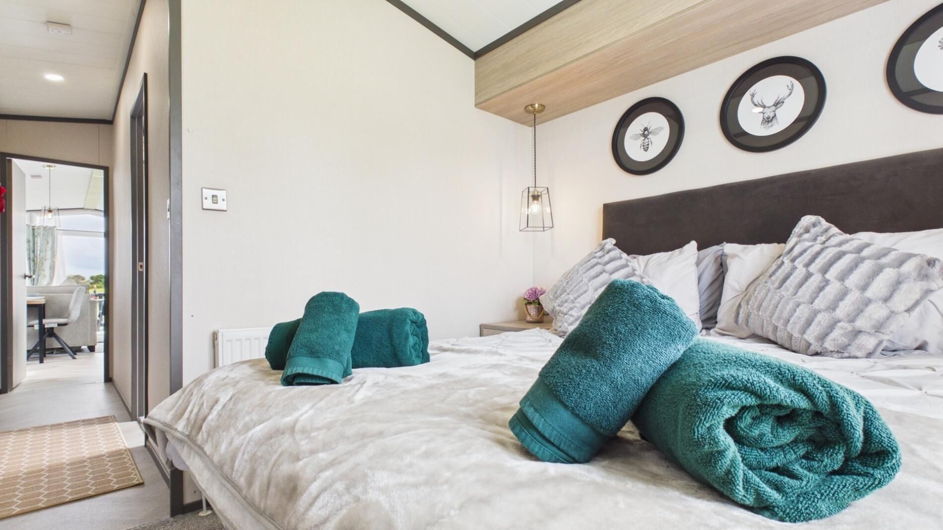 A hotel room with a bed, pillows, a nightstand, a lamp, and a view of the outside.
