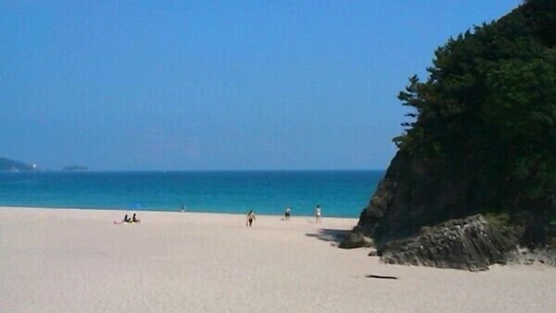 Een strand met een heldere lucht, kalme zee en een rotsachtige klif.