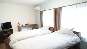 Quarto de hotel com duas camas, televisão, escrivaninha e janela com cortinas.