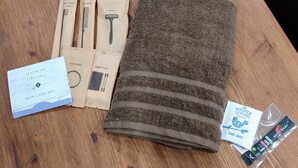 Uma mesa de madeira com uma toalha castanha, um conjunto de cuidados para a pele, elástico de cabelo, nécessaire e produtos de higiene pessoal.