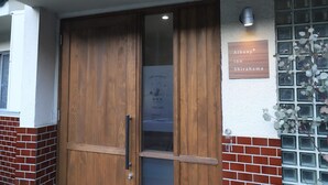 Uma porta de madeira com um painel de vidro, uma placa indicando "Albany Inn Shirahama" e uma parede de tijolos com uma janela.