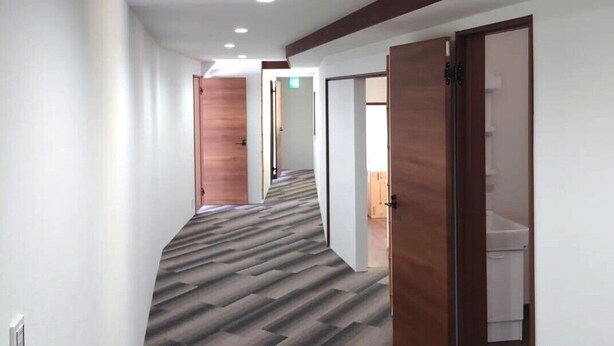 Um corredor com piso coberto por carpete, portas de madeira e luminárias embutidas no teto.