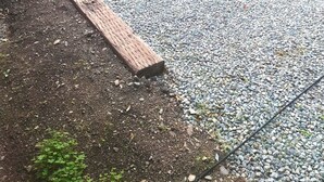 Uma área pavimentada com tábuas de madeira e pedriscos, rodeada por vegetação e uma placa.