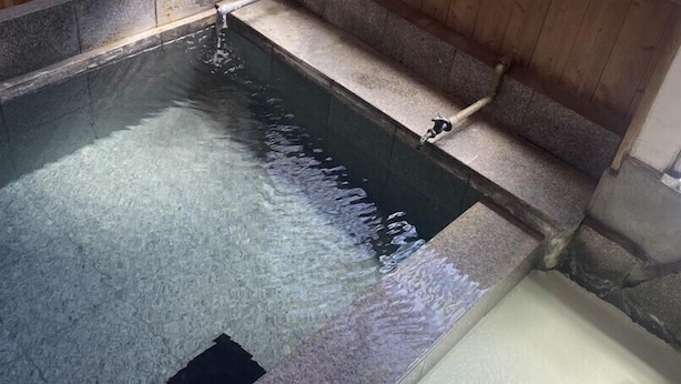 Een stenen zwembad met stromend water, omringd door stenen muren en een houten vloer.