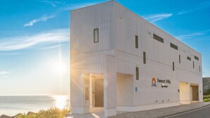 Un bâtiment moderne doté d’un toit plat, de grandes fenêtres et d’une enseigne indiquant « Sunset Villa Spa Resort ».
