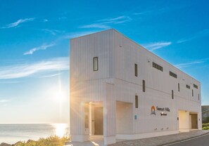 Un bâtiment moderne doté d’un toit plat, de grandes fenêtres et d’une enseigne indiquant « Sunset Villa Spa Resort ».
