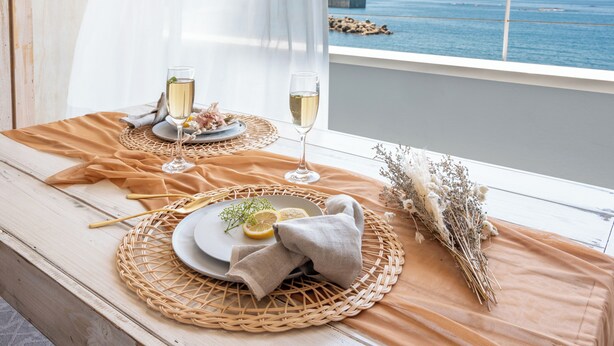 Une table dressée avec des assiettes, des verres et un bouquet de fleurs, donnant sur une étendue d’eau.
