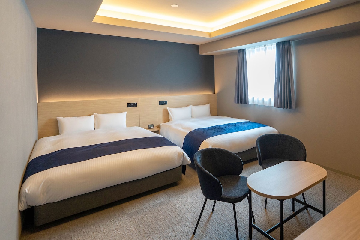 Habitación de hotel con dos camas, un escritorio y una silla.