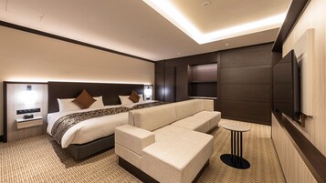 Una habitación de hotel moderna con una cama grande, un sofá, un televisor y una mesita.