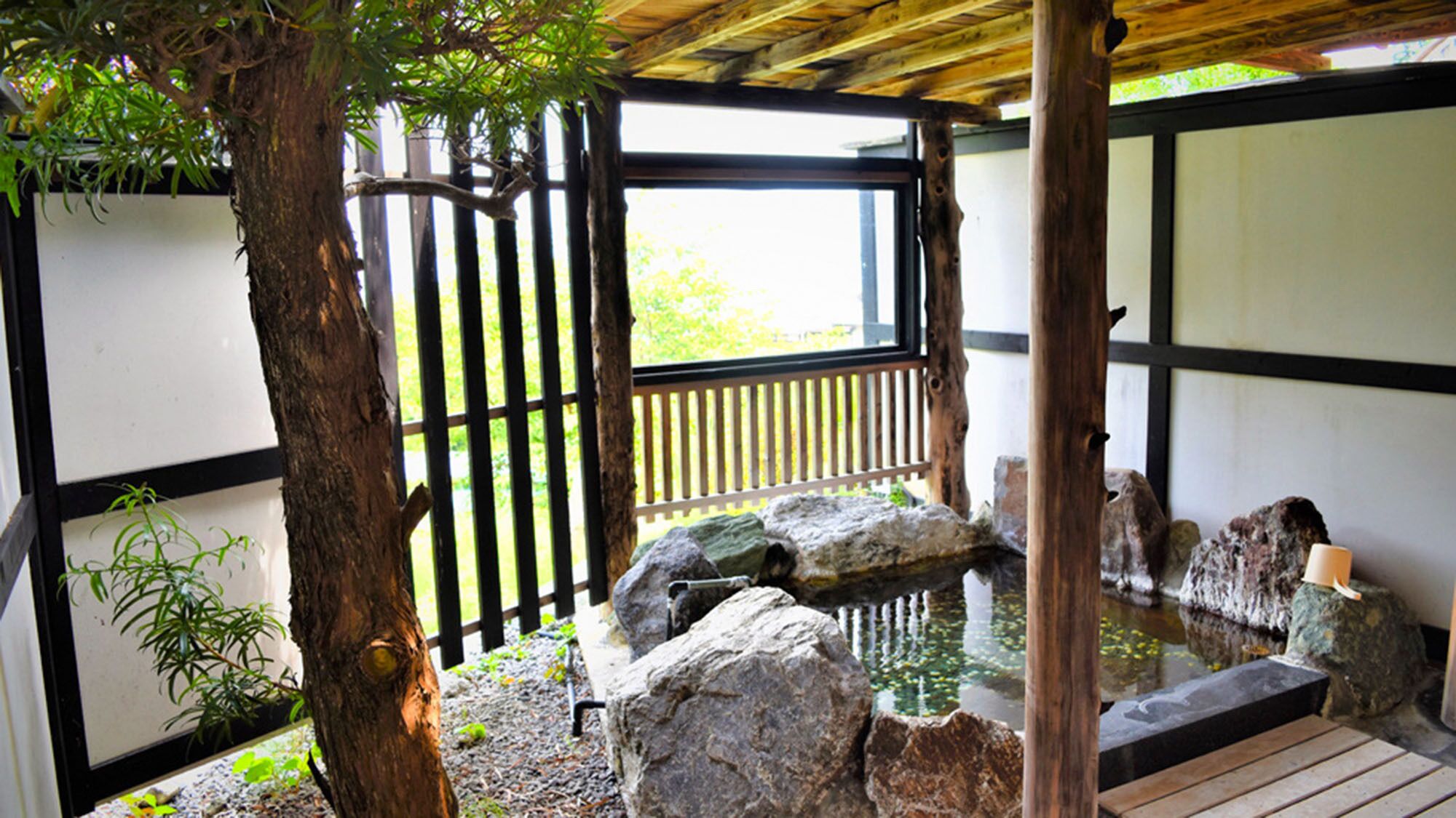 A traditional Japanese garden with a wooden deck, rock formations, and a small pond.